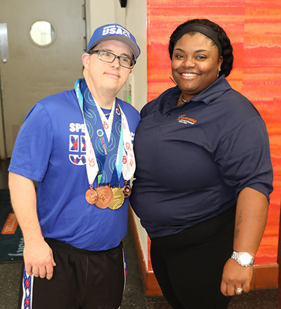 Man with Down Syndrome wearing special olympics medals standing next to Employment Specialist