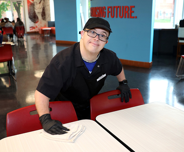 A man with Down Syndrome cleaning table in a college cafeteria 