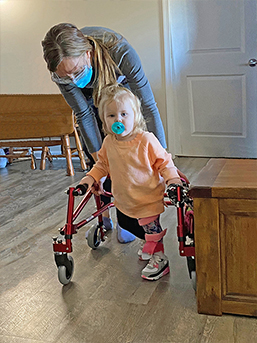 Toddler Everleigh walks with the help of a walker and Easterseals therapist