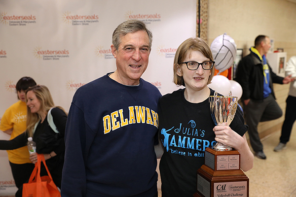 Governor Carney standing with person with disability who is holding a trophy in front of an Easterseals step and repeat