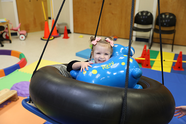 Child in physical therapy swing holding a toy in a colorful room