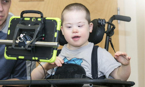 A young boy with down syndrome smiles and uses a tablet