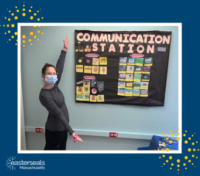 speech language therapist with mask on standing next to her communication board