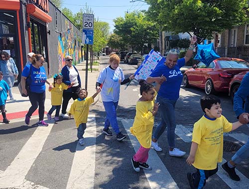 group of adults and children crossing a city street. Most are wearing blue shirts in support of autism acceptance.