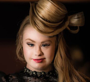 White woman with Down Syndrome, her hair up and stylized in a very ostentatious, fashionable way