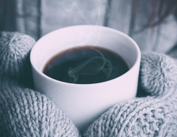 a close up of a steaming mug of tea, held by hands with mittens