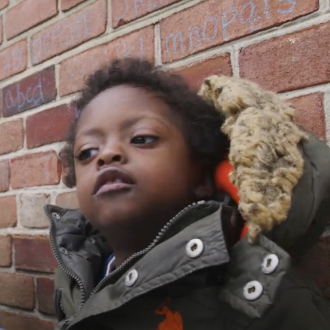 Langston wearing a coat and sitting against a brick wall outside