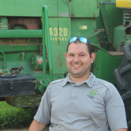 young adult male, Cade, smiling in front of a green tractor
