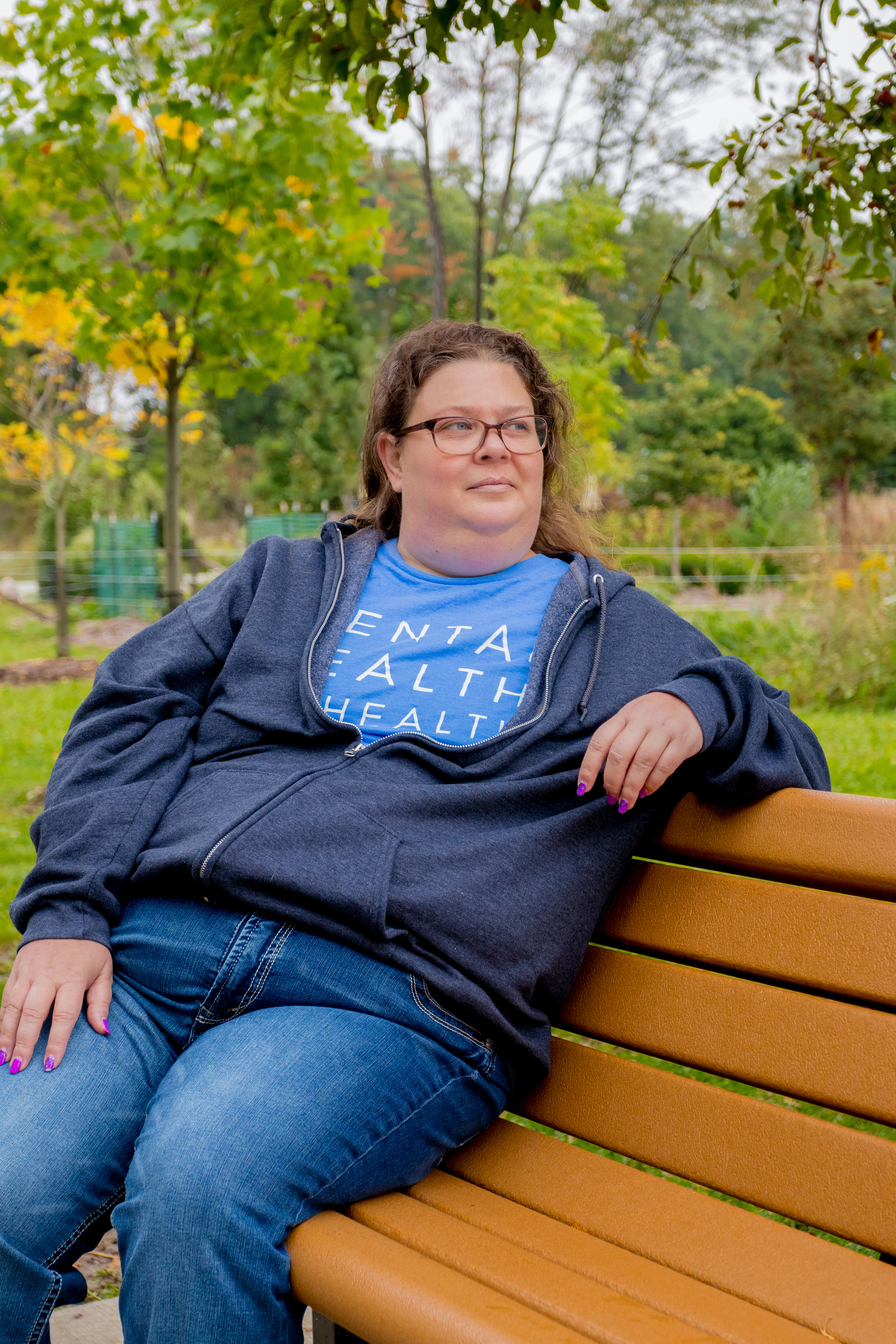 Jenn sitting on a bench at a park and looking off in the distance 