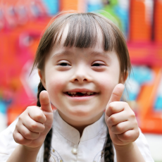 a young girl smiling at the camera and giving two thumbs up