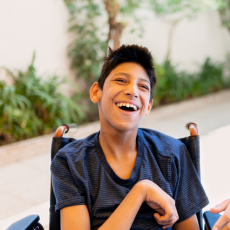 a teen boy who uses a wheelchair smiles at the camera