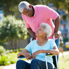 a woman using a wheelchair and a man pushing her look at eachother, they are outside.