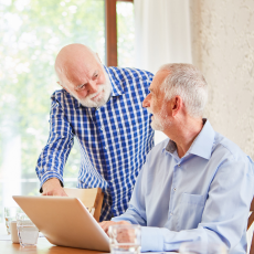 two older men at a table and looking at the computer