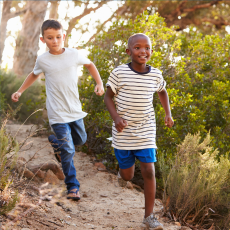 a photo of two boys running and playing outside among trees and bushes.