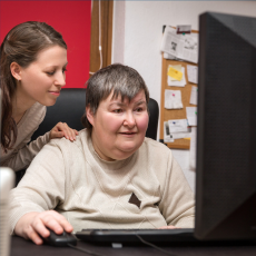 two women looking at a computer, one woman has her hand on the other woman's shoulder.