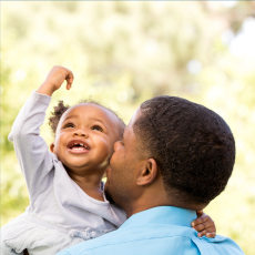 A young girl being held by her father and smiling.