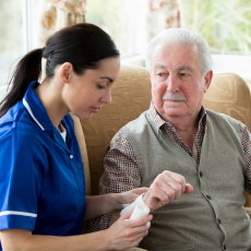 A nurse sits next to an older man, providing treatment. 