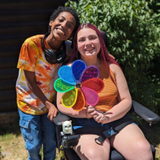 a camper and counselor holding a rainbow pinwheel and smiling