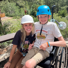 a photo of a counselor and camper in a wheelchair wearing helmets at the climbing wall