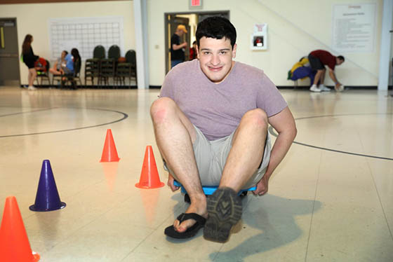 A Young man sitting on a rolling device in a gym looking at the camera.