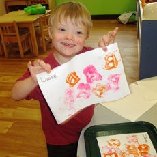 little boy smiling holding up a piece of his artwork