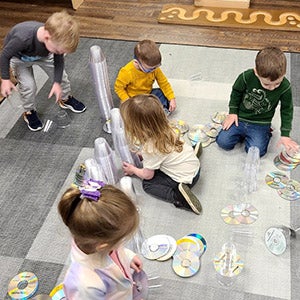 Gavin with friends on the floor doing a project with DVDs and plasticware