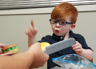 Caydence signing at an object during therapy