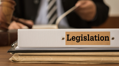 notebook with word legislation printed on it with a blurred backdrop of a judge at a desk