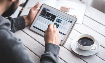 close up of someone looking up information on a tablet next to a cup of coffee