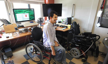 A young man sits in his wheelchair at an adapted computer setup