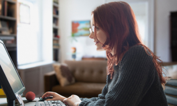 a woman sits at a desk using a computer inside her apartment