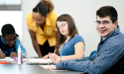 a young man sits at a table with other students and smiles