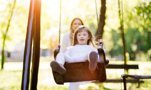 a young girl with Down syndrome swings while being pushed by an adult