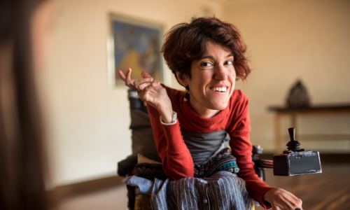 a woman with a disability smiles at the camera while sitting in her electronic wheelchair
