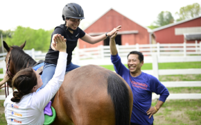 a person riding a horse high fives a man and woman with a barn in the background