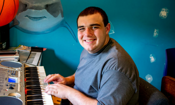 young man sitting at a piano with a blue wall behind him