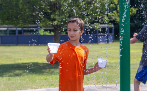 a young boy plays with a water cup on a splash pad outside