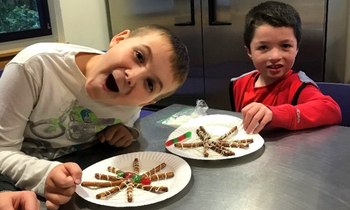 two young boys smiling while sitting at a table with a homemade snack