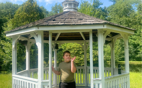 a young boy smiles standing underneath a gazebo surrounded by greenery