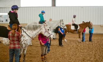 a group of people take an adaptive riding lesson in an indoor arena
