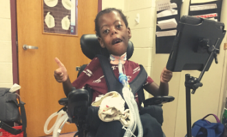Young child in a wheel chair with his iPad gesturing a thumbs up