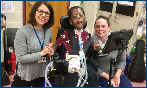 young black boy in a wheel chair smiling with his two aides
