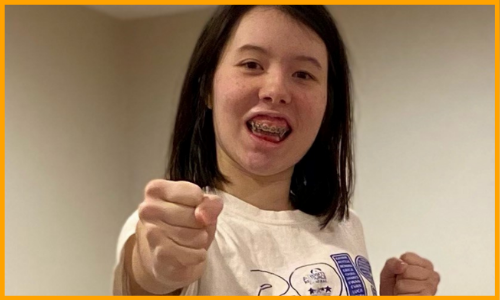 Naomi smiles and holds out her fists in a martial arts pose