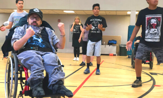 A man in a wheelchair participates in an accessible martial arts class, holding out his fists