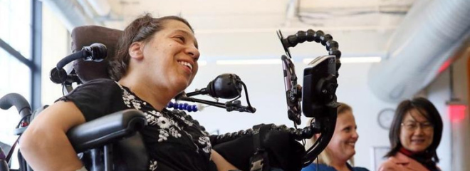 a woman sits in a wheelchair with assistive technology attachments and smiles