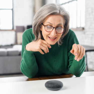 A woman leans on a counter and uses a voice assistant device