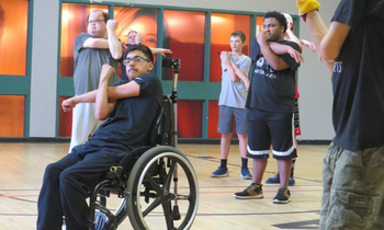 a group of people sit, stand, and stretch in Accessible Martial Arts class