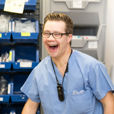 A young man with a disability smiles at work in a medical setting while wearing scrubs