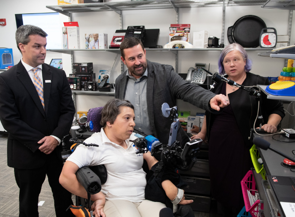 adult woman in a wheel chair showing other adults a virtual remote at a technology center