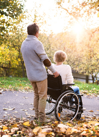 a person stands with a person sitting in a wheelchair on an autumn day